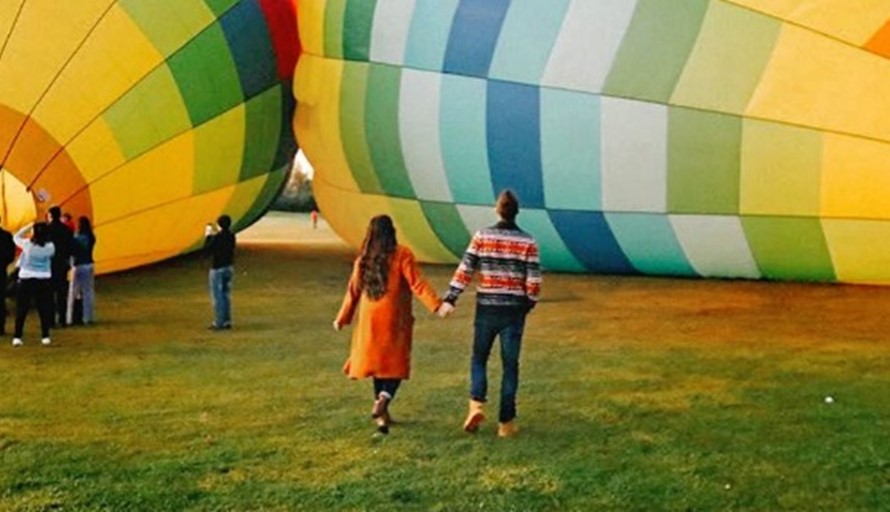 married couple holding hands walking to expensive wedding gift of a hot air balloon ride